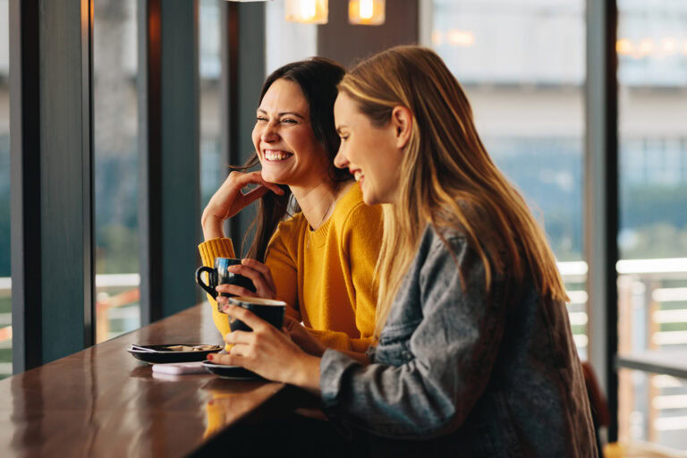 Zwei Frauen genießen Kaffee und lachen in einem modernen Café.